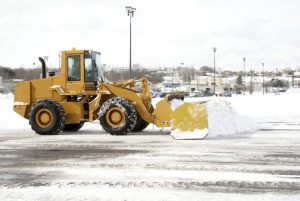 A large yellow earth mover plowing snow after a blizzard